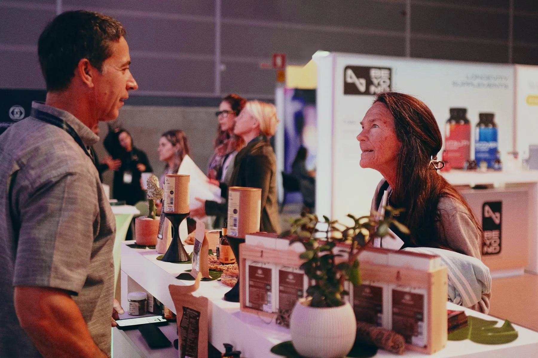 A visitor talking with an exhibitor across a table of health products in the exhibition, 2025